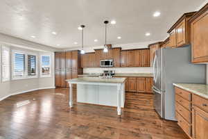 Kitchen with stainless steel appliances, a kitchen island with sink, hanging light fixtures, light stone counters, and a breakfast bar