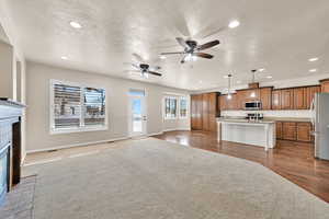 Kitchen with a center island with sink, ceiling fan, appliances with stainless steel finishes, a fireplace, and hanging light fixtures