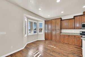 Kitchen with dark wood-type flooring, stainless steel appliances, and light stone counters