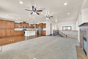 Unfurnished living room with ceiling fan, a tiled fireplace, and dark colored carpet