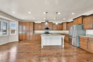 Kitchen featuring an island with sink, appliances with stainless steel finishes, decorative light fixtures, light stone countertops, and sink