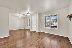 Empty room with a textured ceiling, dark hardwood / wood-style floors, and a notable chandelier