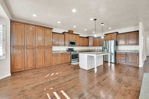 Kitchen with light stone countertops, pendant lighting, stainless steel appliances, an island with sink, and a kitchen breakfast bar