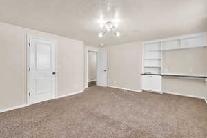 Unfurnished bedroom with carpet, a textured ceiling, and a notable chandelier