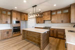 Kitchen featuring hanging light fixtures, a kitchen island, stainless steel appliances, light stone countertops, and light hardwood / wood-style floors