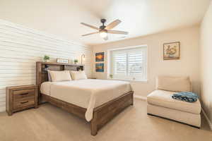 Bedroom with light carpet, baseboards, wood walls, and ceiling fan