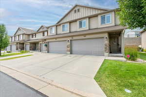 Townhome / multi-family property featuring board and batten siding, an attached garage, driveway, a front yard, and stone siding