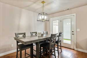Dining space with dark wood-style floors, healthy amount of natural light, and a chandelier
