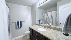 Bathroom featuring toilet, vanity, a shower with curtain, and tile patterned floors