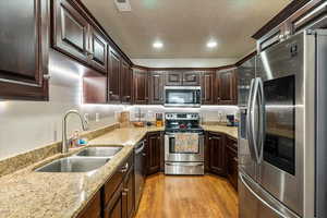 Kitchen featuring stainless steel appliances, light wood finished floors, recessed lighting, dark brown cabinets, and light stone countertops