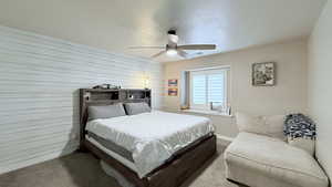 Bedroom featuring ceiling fan, carpet floors, and wooden walls