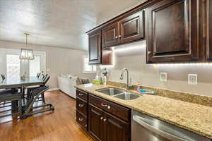 Kitchen with dishwasher, dark wood-style flooring, dark brown cabinetry, a textured ceiling, and pendant lighting