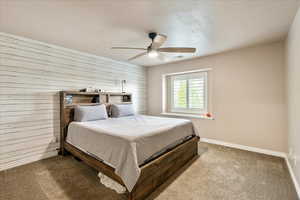 Carpeted bedroom featuring wood walls and a ceiling fan