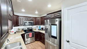 Kitchen featuring light hardwood / wood-style flooring, stainless steel appliances, dark brown cabinets, and light stone counters