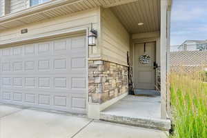 View of exterior entry with stone siding, a garage, and concrete driveway