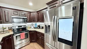 Kitchen with light stone countertops, dark brown cabinets, stainless steel appliances, and light hardwood / wood-style floors