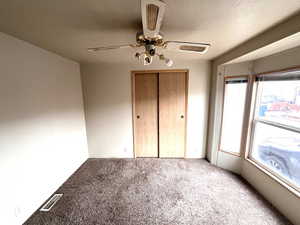 Unfurnished bedroom with ceiling fan, a textured ceiling, a closet, and carpet flooring