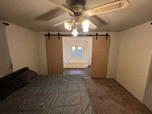 Unfurnished bedroom featuring ceiling fan, a barn door, a textured ceiling, and ensuite bath