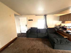 Living room featuring ornamental molding, lofted ceiling, and dark carpet