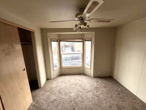 Unfurnished bedroom with carpet floors, ceiling fan, a closet, and a textured ceiling