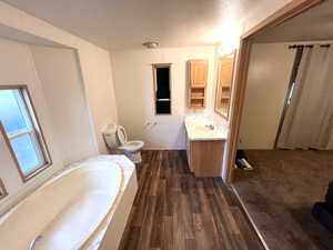 Bathroom with toilet, vanity, a bath, hardwood / wood-style flooring, and a textured ceiling