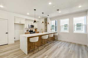 Kitchen featuring white cabinetry, hanging light fixtures, light stone counters, light hardwood / wood-style floors, and stainless steel appliances