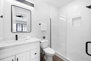 Bathroom featuring toilet, a shower with shower door, ceiling fan, wood-type flooring, and vanity