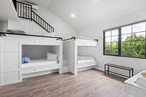 Unfurnished bedroom with lofted ceiling, light hardwood / wood-style floors, and an AC wall unit