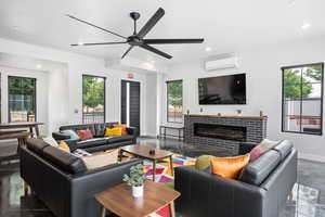 Living room featuring a brick fireplace, a healthy amount of sunlight, an AC wall unit, and ceiling fan