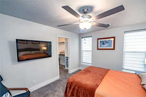 upstairs apartment over detached garage: Bedroom featuring a textured ceiling, a walk in closet, dark colored carpet, a closet, and ceiling fan