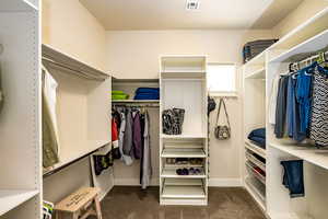 Spacious owner's walk-in closet with dark colored carpet