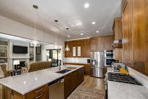 Kitchen with stainless steel appliances, sink, hanging light fixtures, a kitchen island with sink, and light counters