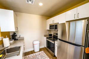 upstairs apartment over detached garage: Kitchen with stainless steel appliances, light hardwood / wood-style floors, white cabinets, and sink