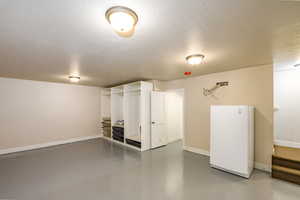 Basement with a textured ceiling and white freezer with storage closets.