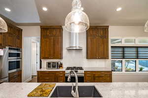 Kitchen with stainless steel appliances, wall chimney range hood, a textured ceiling, pendant lighting, and sink