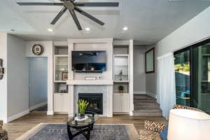 Family room with a textured ceiling, dark wood-type flooring, a tiled fireplace, and ceiling fan