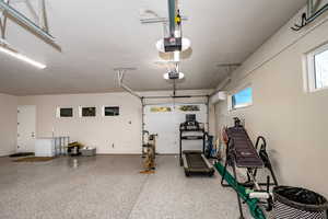 Garage w/ epoxy flooring featuring an AC wall unit and a garage door opener with drive through garage door bay to backyard area.