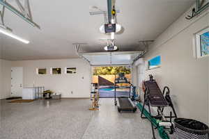 Garage w/ epoxy flooring featuring an AC wall unit and a garage door opener with drive through garage door bay to backyard area.