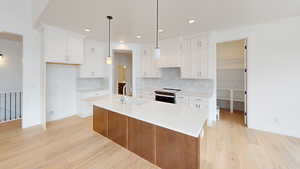 Kitchen featuring stainless steel range with electric cooktop, a sink, a center island with sink, and white cabinetry