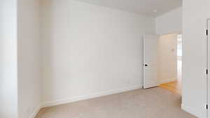Unfurnished room featuring light carpet and baseboards