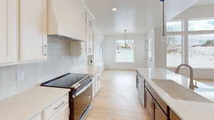 Kitchen featuring white cabinetry, custom range hood, appliances with stainless steel finishes, and decorative light fixtures
