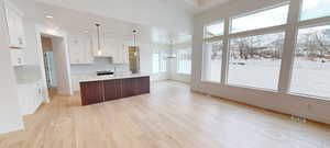 Kitchen with light wood finished floors, a center island with sink, visible vents, light countertops, and white cabinetry