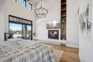 Bedroom featuring a towering ceiling, a chandelier, baseboards, wood finished floors, and a tile fireplace