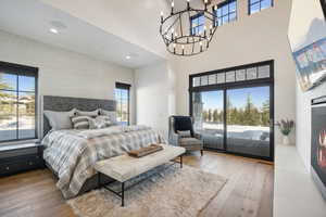 Bedroom with access to outside, a high ceiling, an inviting chandelier, and hardwood / wood-style flooring