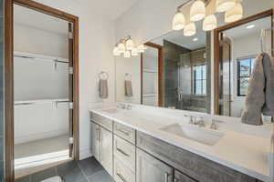 Full bath with double vanity, a tile shower, and a walk in closet