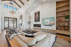 Living room with high vaulted ceiling, recessed lighting, beam ceiling, hardwood / wood-style floors, and a glass covered fireplace