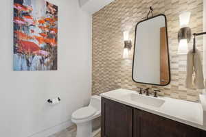 Bathroom featuring vanity, toilet, and decorative backsplash
