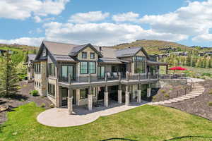 Back of house featuring stone siding, a standing seam roof, a patio, a lawn, and metal roof