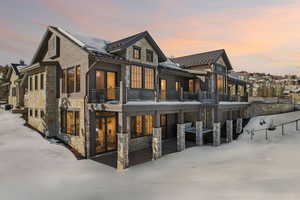 Snow covered house with stone siding, a standing seam roof, a balcony, and metal roof