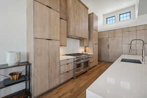 Kitchen with light brown cabinetry, sink, range with two ovens, and hardwood / wood-style flooring